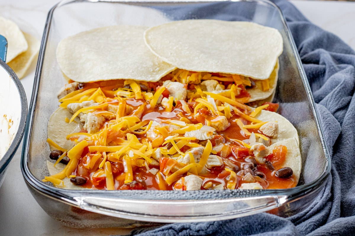a glass baking dish with layers of tortillas, chicken, red enchilada sauce, shredded cheese and black beans