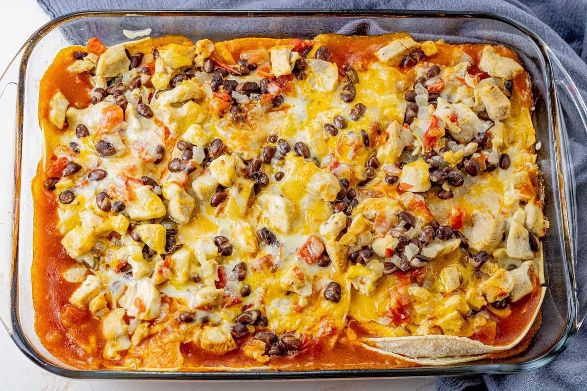 a glass baking dish filled with layers of tortillas, enchilada sauce, chicken, black beans