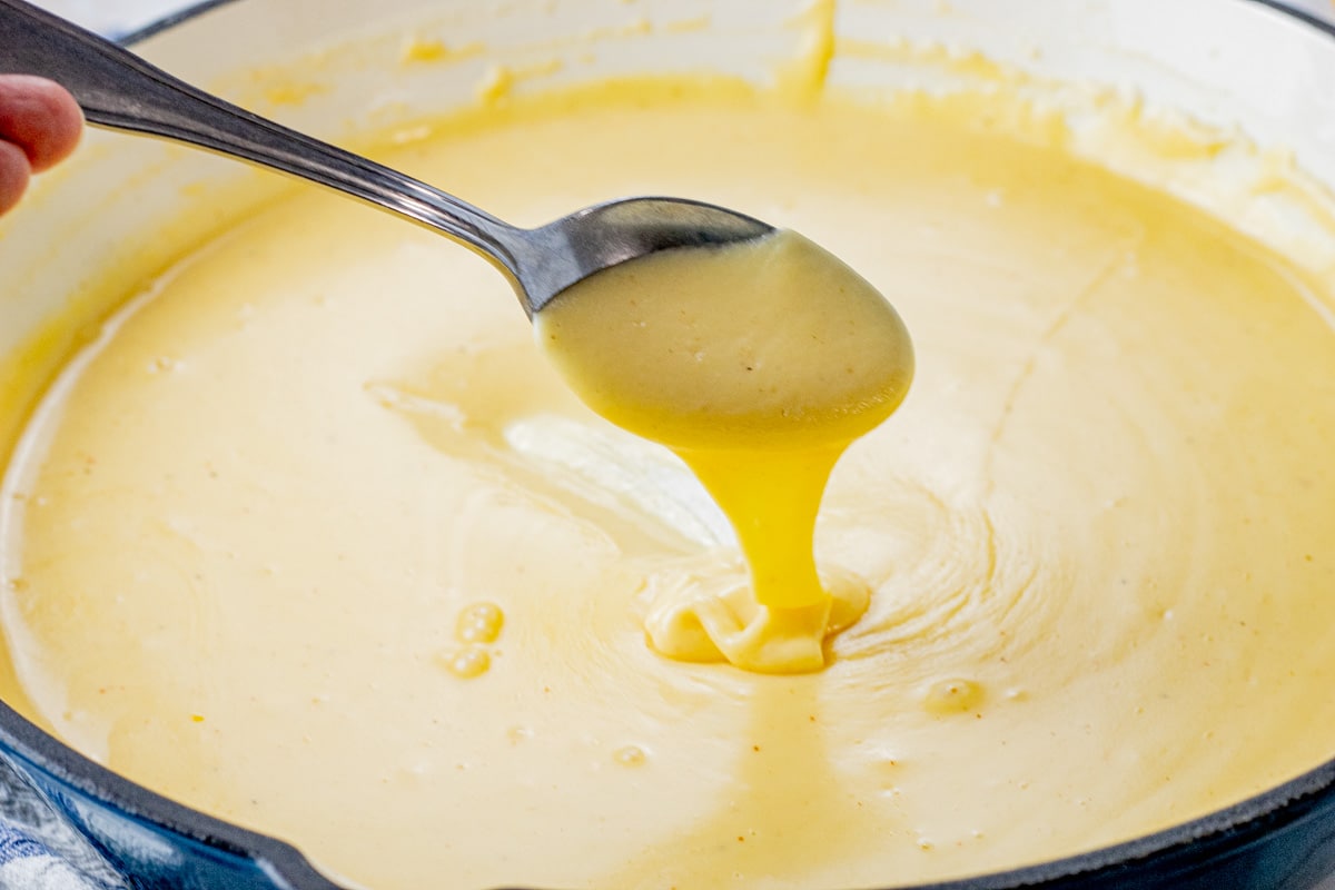 spoon dripping cheese sauce into a pan