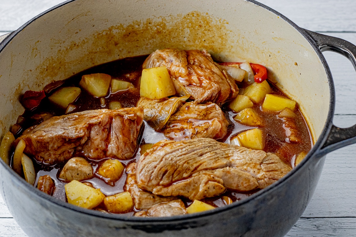 uncooked pork ribs in a pot with pineapples, peppers, onions and bbq sauce
