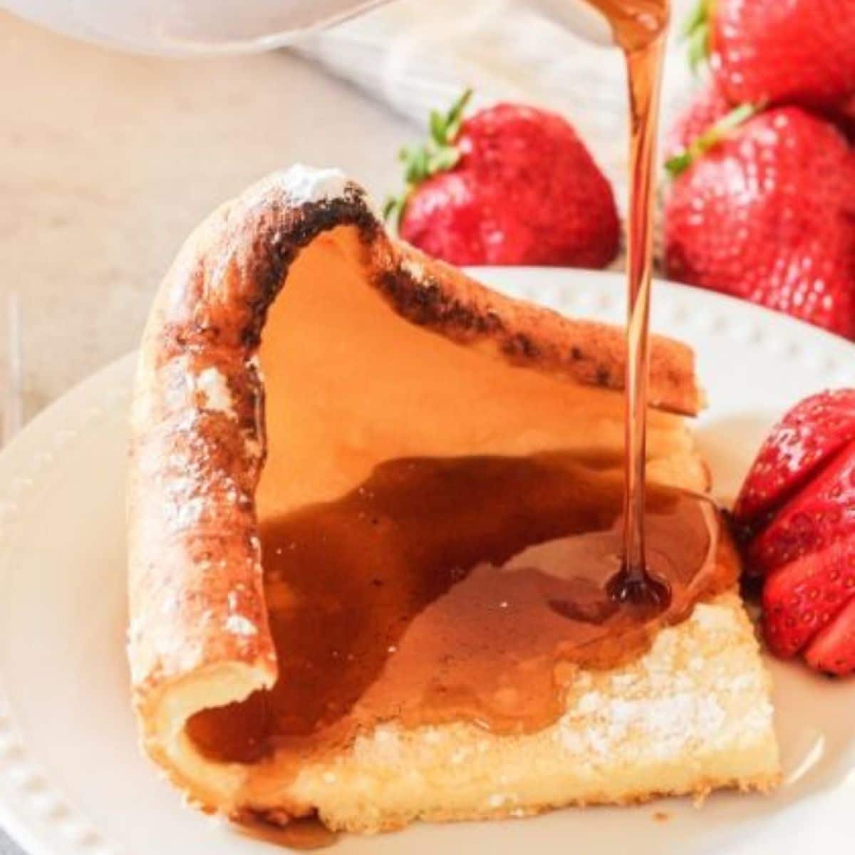 syrup pouring onto a german pancake on a white plate