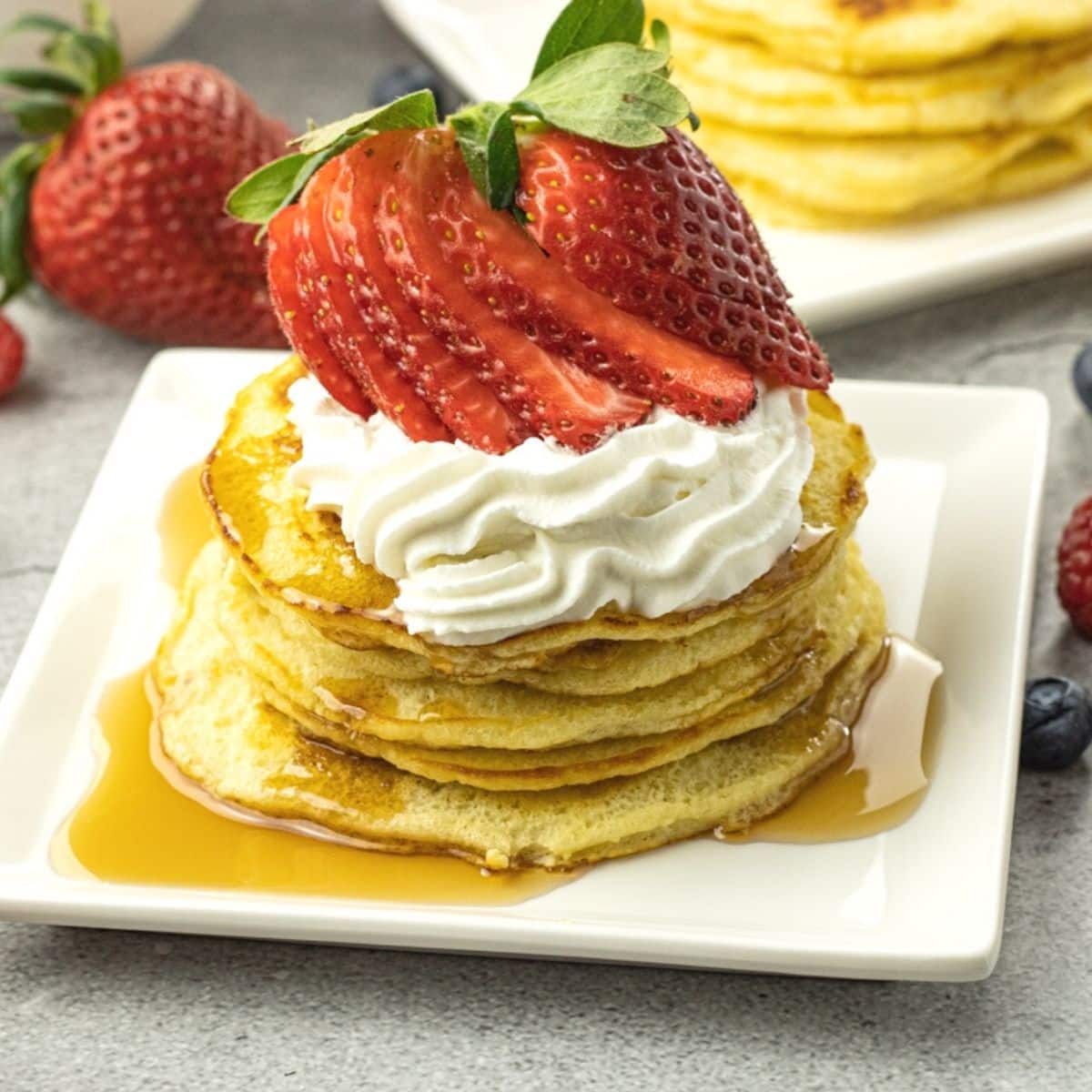 pile of pancakes topped with whipped cream and strawberries