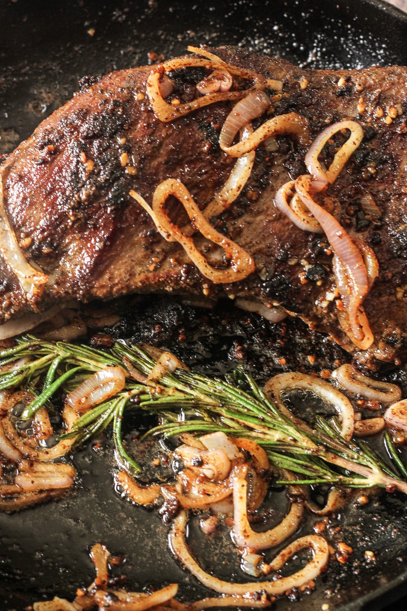 tri tip beef roast cooked in a cast iron pan with onions, rosemary and garlic