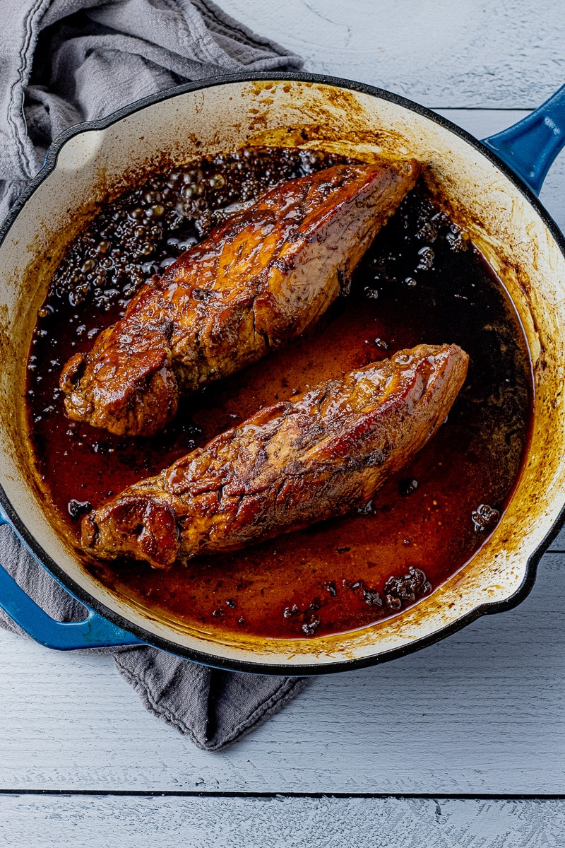 two pork tenderloins in a cast iron pan with a dark maple glaze