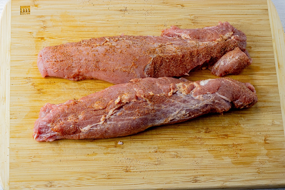 two pork tenderloins uncooked, on a wooden cutting board