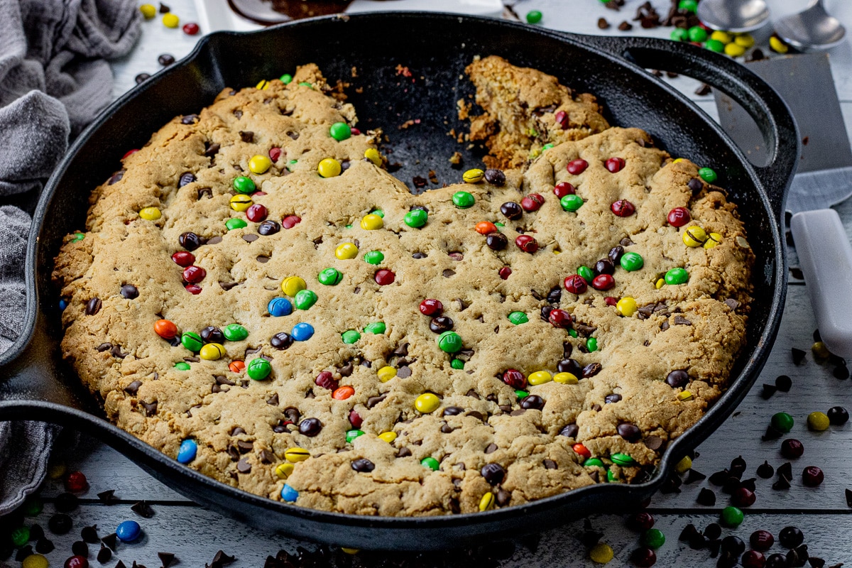 chocolate chip cookie in a large cast iron pan with a piece cut out of the cookie