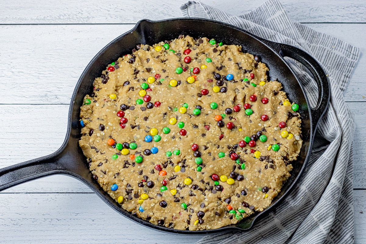 uncooked chocolate chip cookie dough with colorful candies mixed in, pressed into a cast iron pan