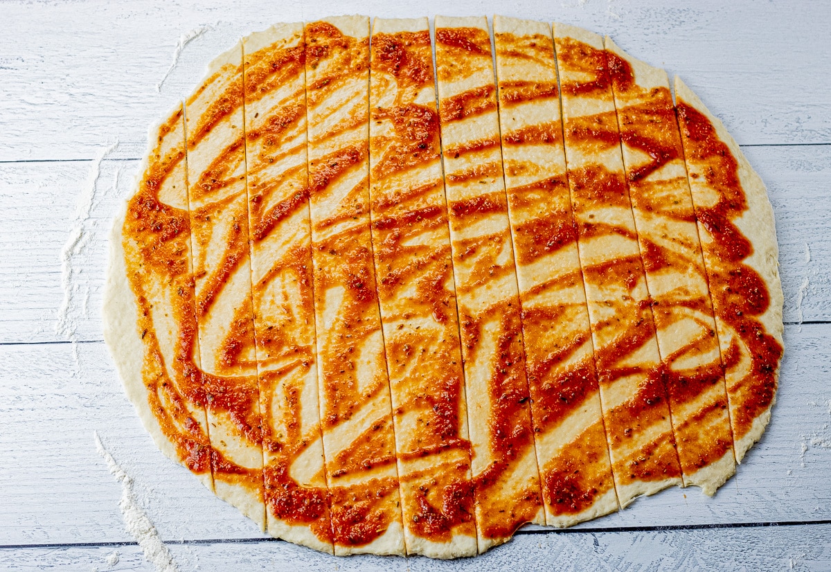 round pizza dough rolled out, topped with pizza sauce and sliced into one inch pieces