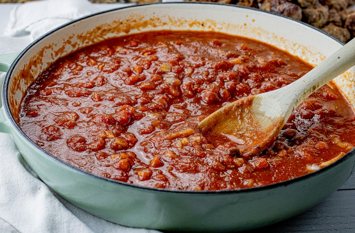 spaghetti sauce in a large, round pan with a wooden spoon sticking out