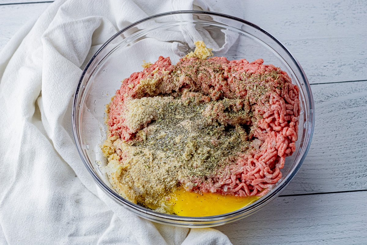 ground beef, egg and spices in a glass mixing bowl