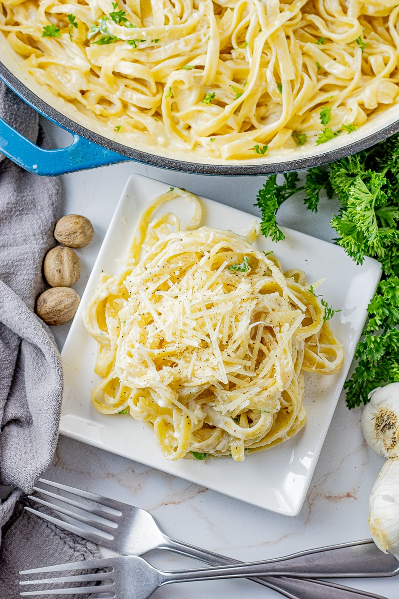 fettucine noodles covered in alfredo sauce in a pile on a white plate