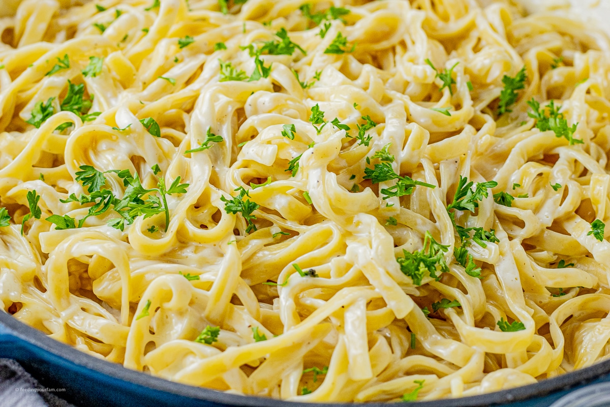 fettucine noodles covered in alfredo sauce and parsley in a large skillet