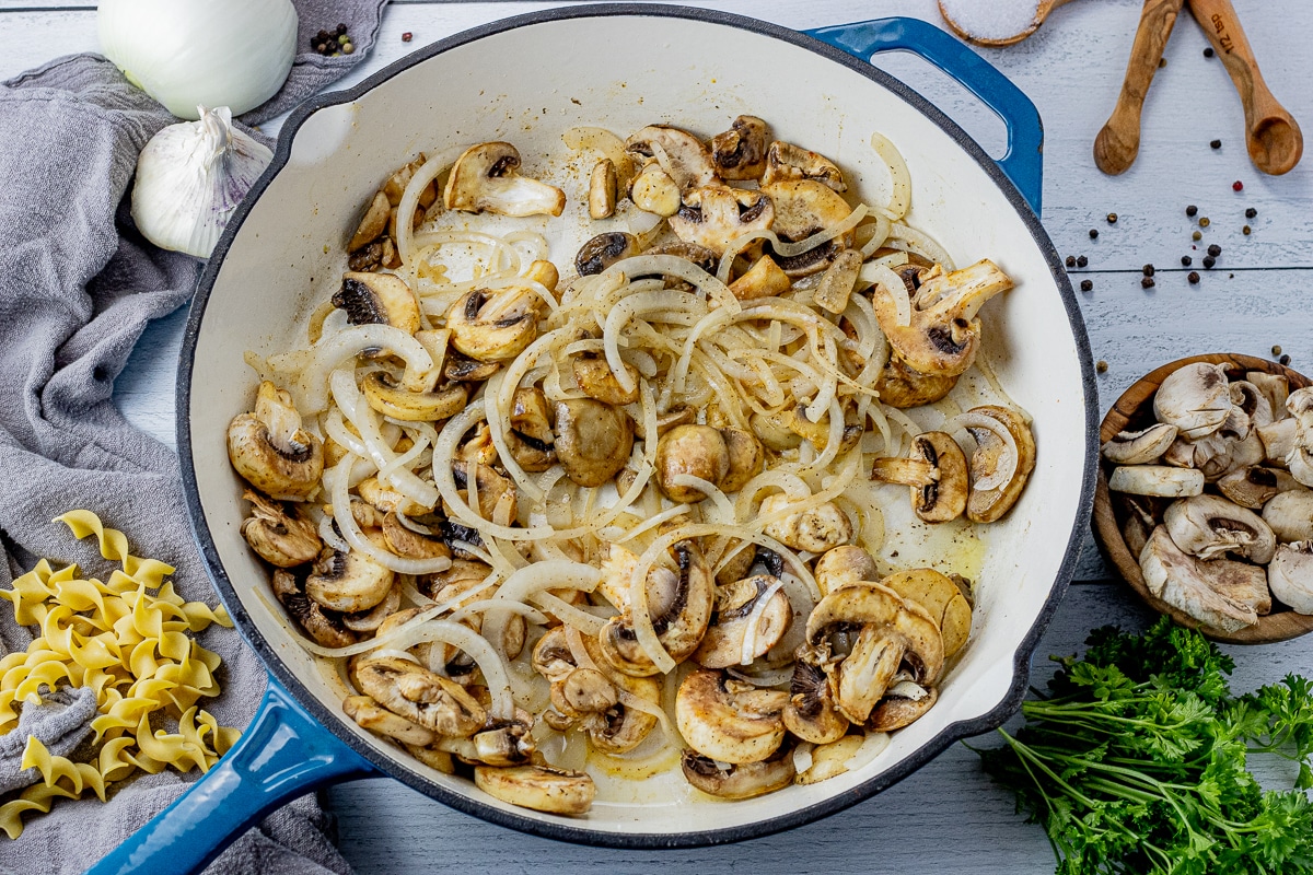 sliced mushrooms and onions cooking in a cast iron pan