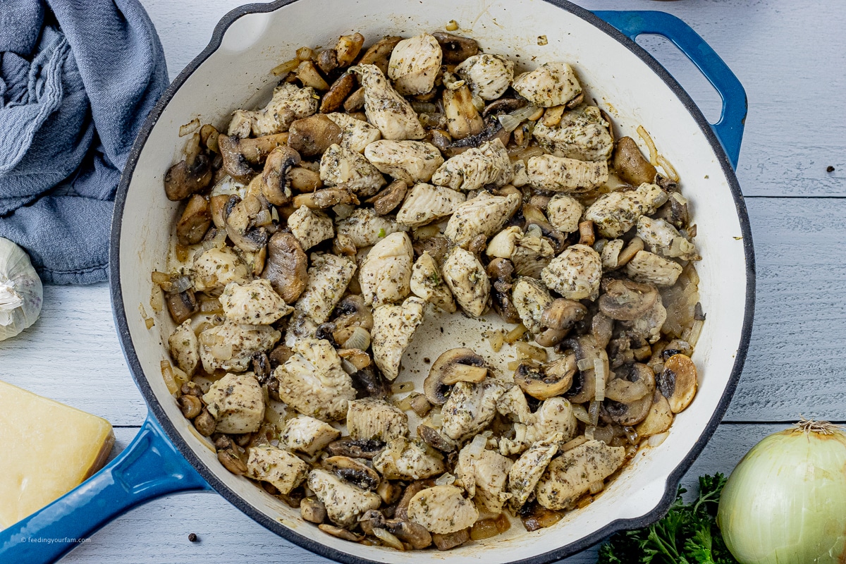 pieces of chicken with mushrooms and sliced onions cooked in a cast iron skillet