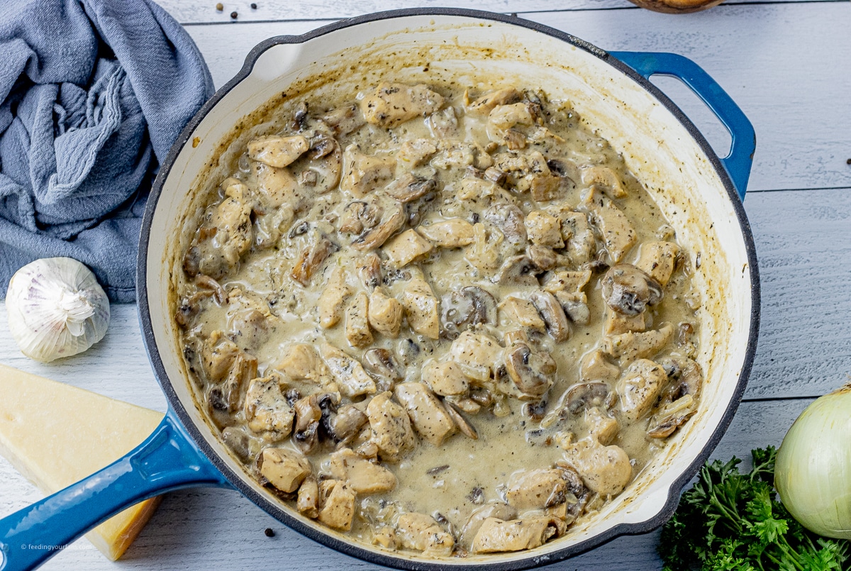chicken with mushrooms and sliced onions in a creamy sauce in a cast iron pan 