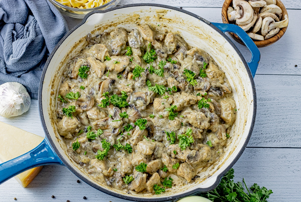 pieces of chicken, mushrooms, sliced onions all in a creamy sauce in a cast iron pan