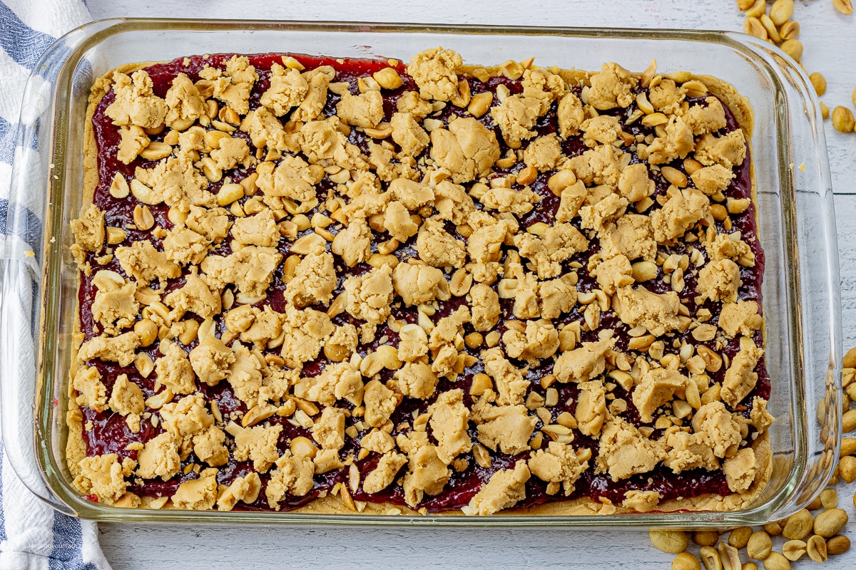 peanut butter cookie dough pressed into a glass 9 x 13 inch baking dish with a layer of raspberry jam and pieces of peanut butter cookie dough on top