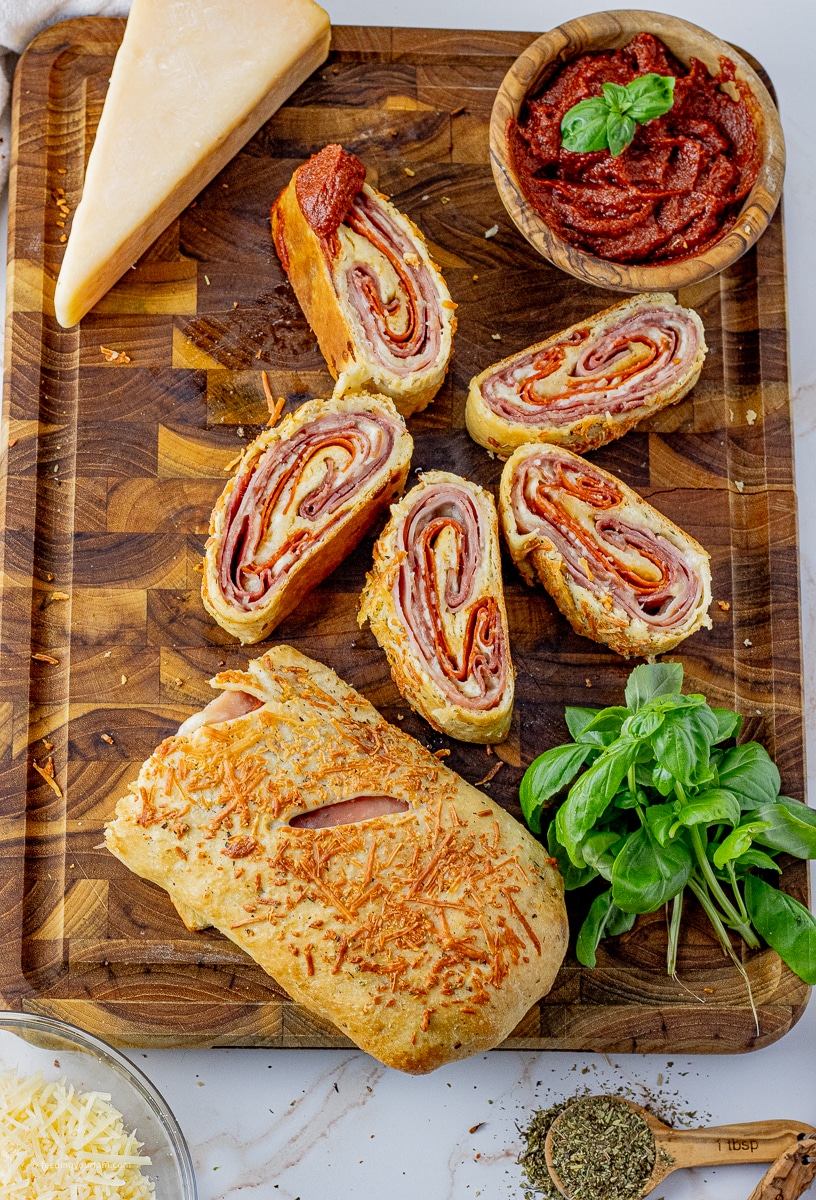 stromboli sliced in half next to 5 smaller slices with pizza sauce on a wooden cutting board