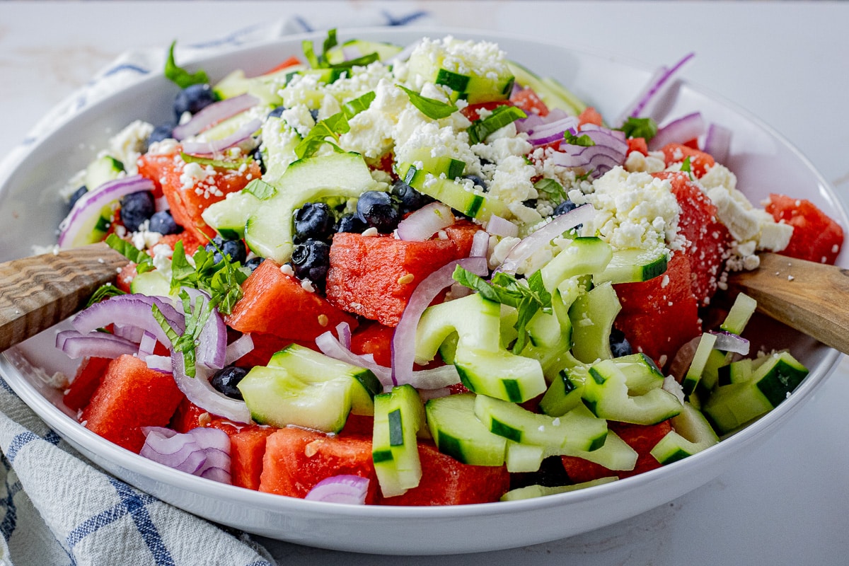 sliced cucumbers, red onions, watermelon and feta cheese in a large white bowl