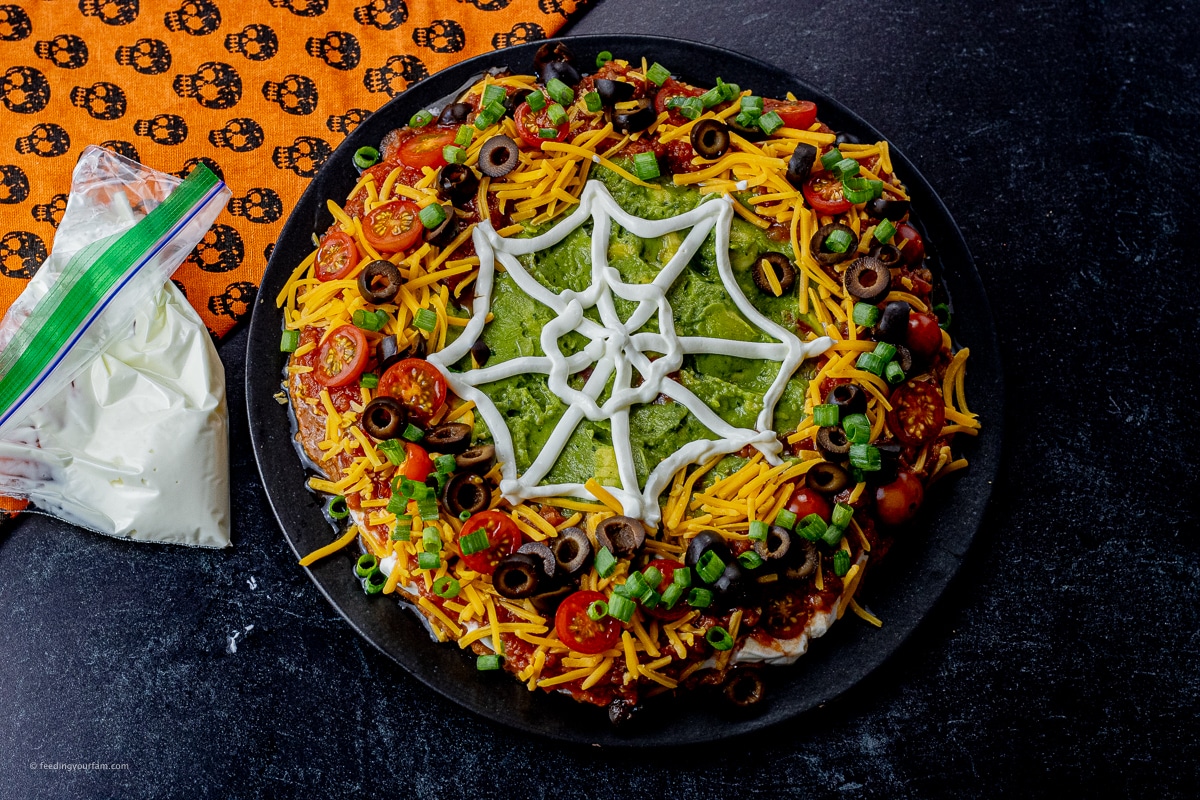 halloween layered dip with a spider web made out of sour cream on top