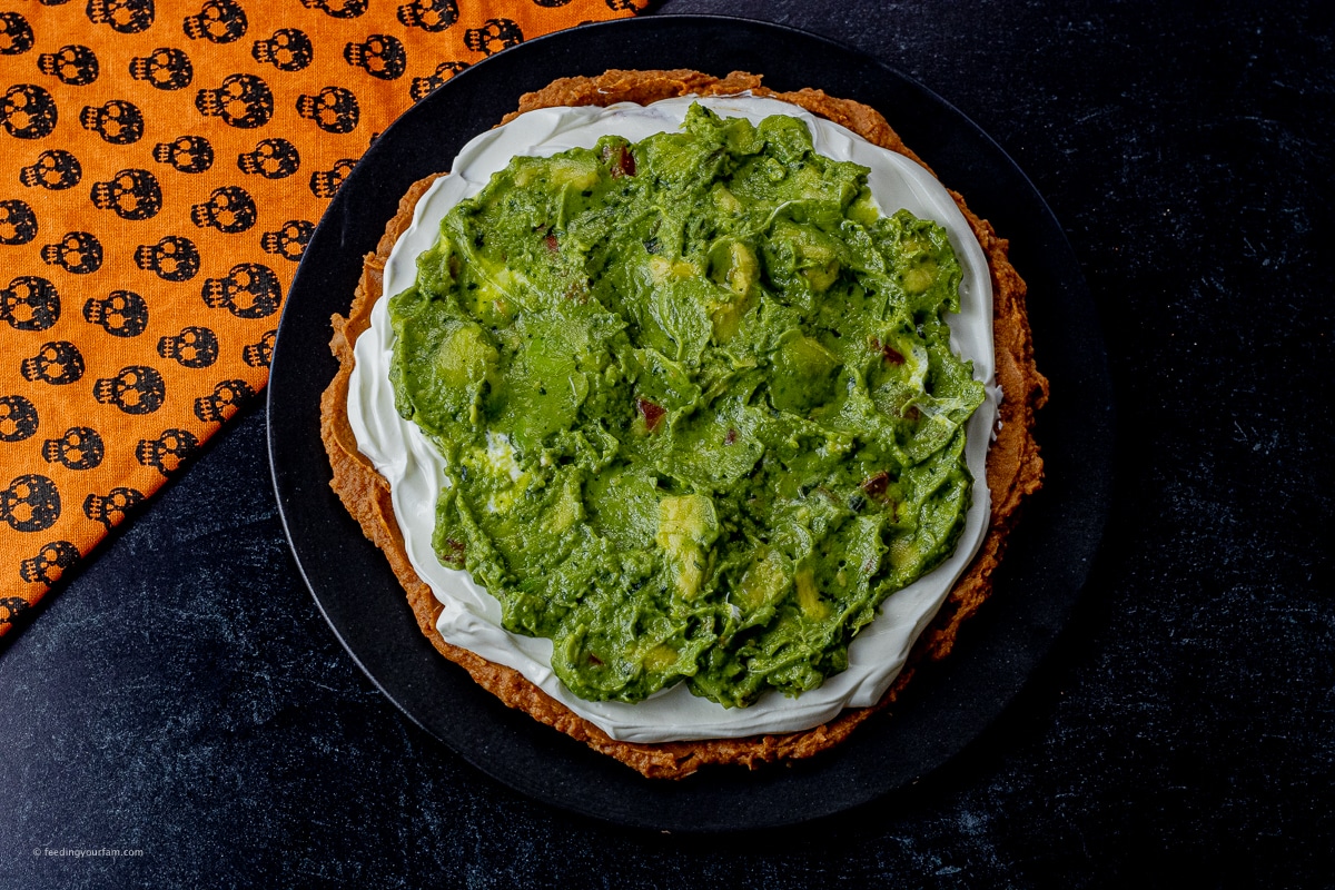 layer of refried beans, sour cream and guacamole on a black plate