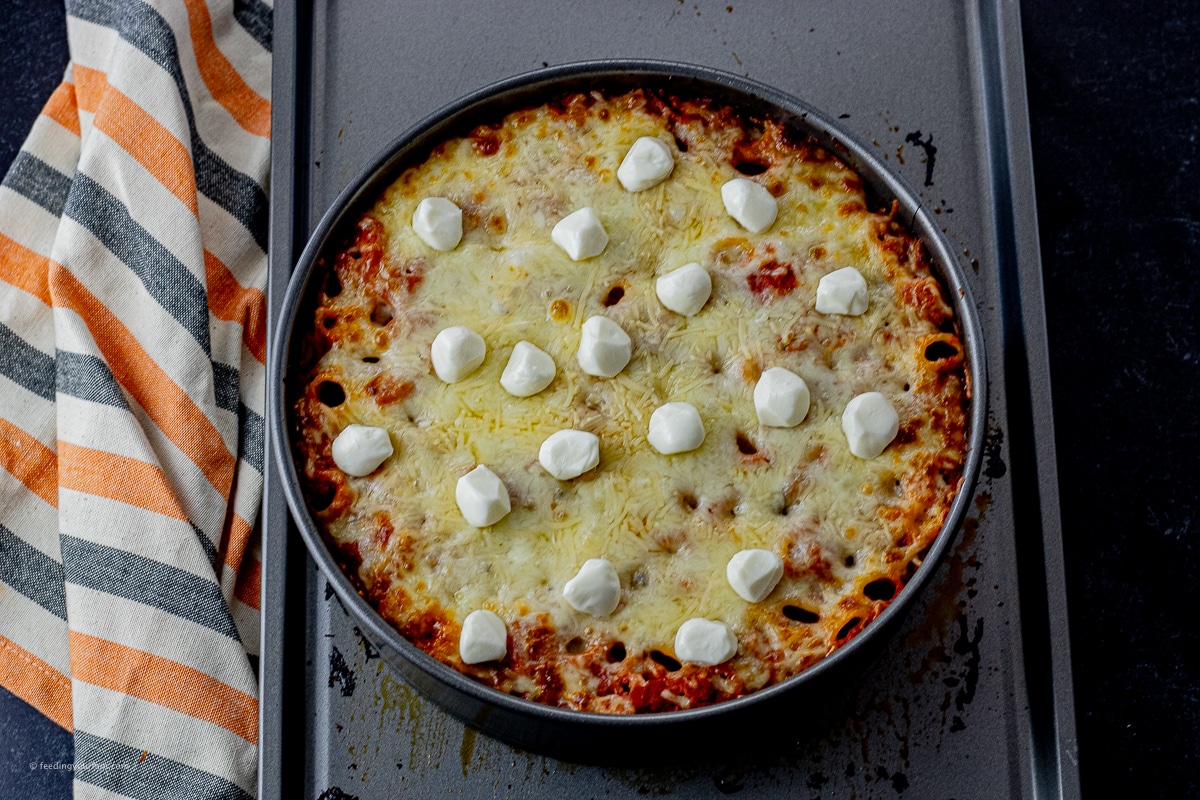 baked rigatoni in a round, springform pan, cooked with cheese on top, then topped with small mozzarella pearls