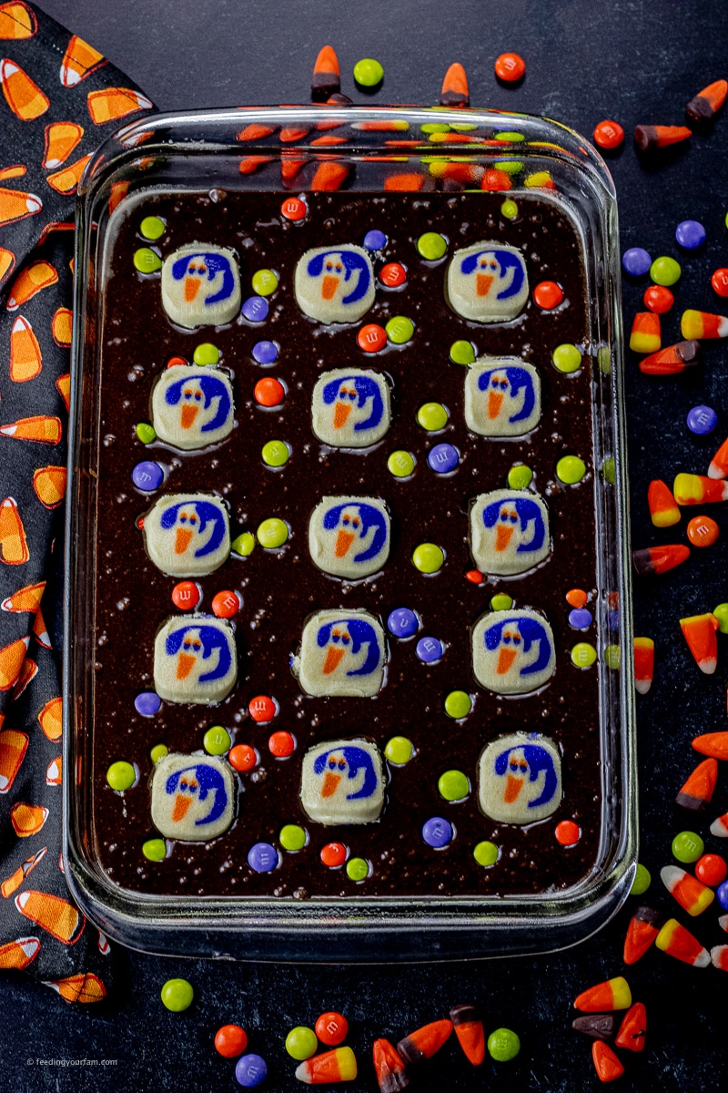 brownie batter topped with ghost sugar cookies uncooked in a glass baking dish