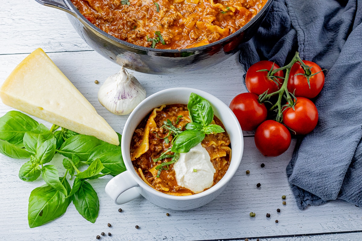 lasagna soup in a white bowl topped with ricotta cheese and fresh basil