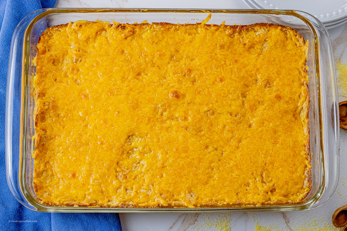 corn casserole topped with cheese in a glass baking dish