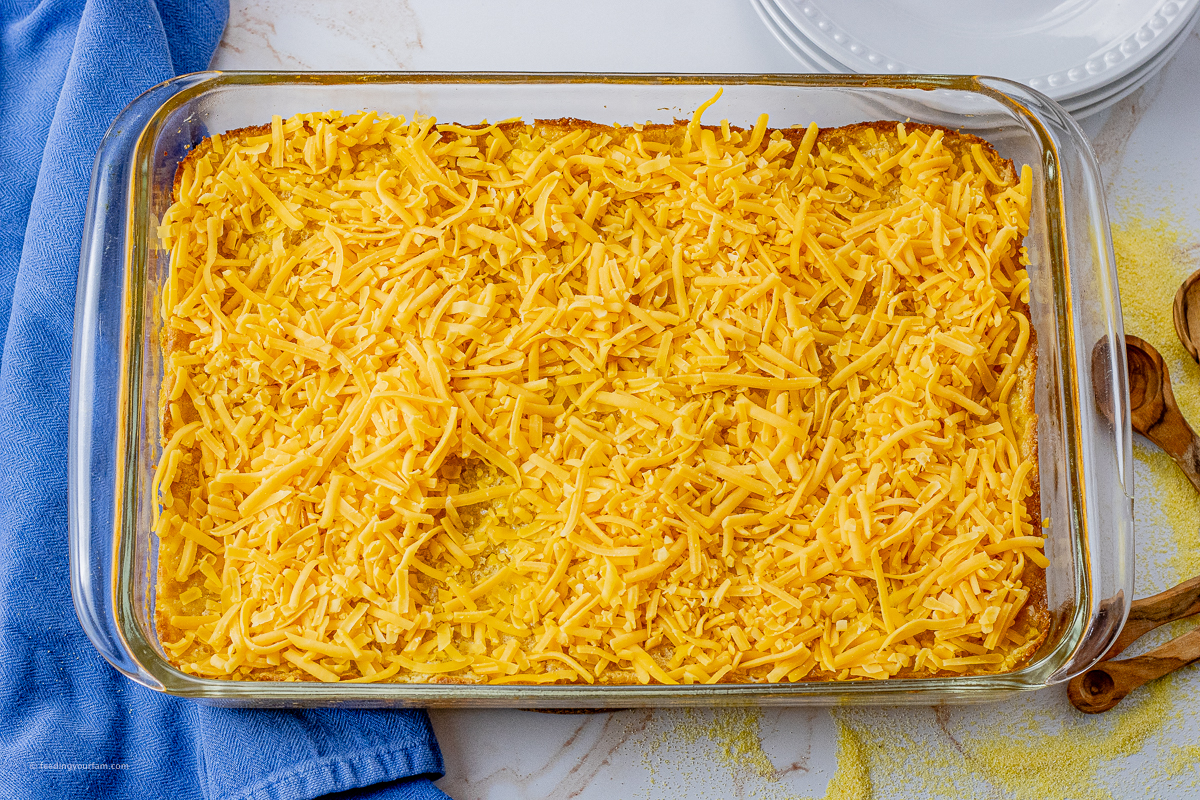 cooked corn casserole topped with cheese in a glass baking pan
