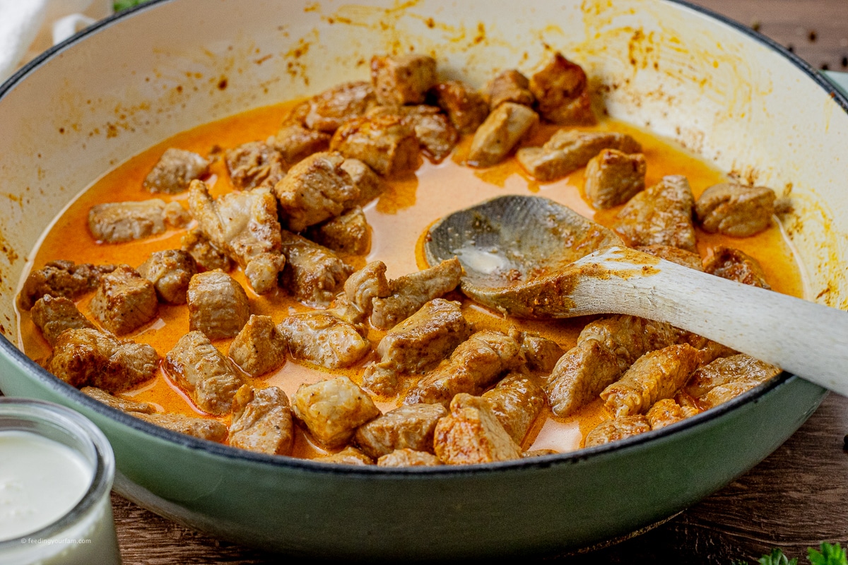 pieces of pork tenderloin cooking in a cream sauce in a large pan