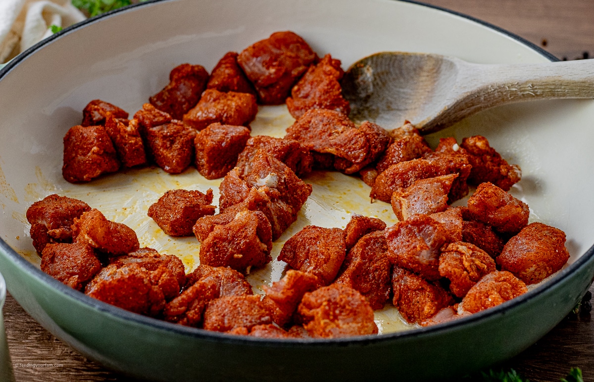 pieces of pork coated in a paprika spice mixture cooking in a large skillet