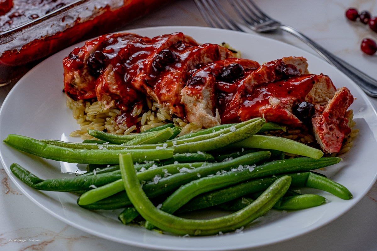 sliced chicken in a cranberry sauce on top of rice with a side of green beans
