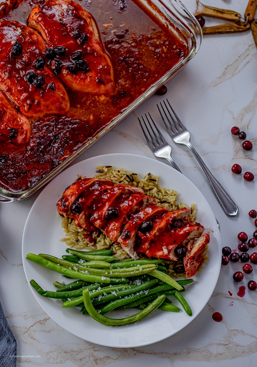 chicken breasts cooked in a cranberry sauce on top of rice with a side of green beans