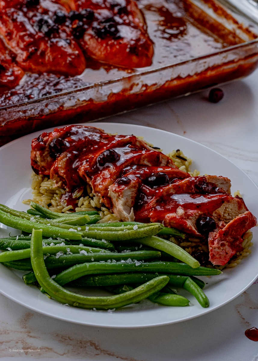 sliced chicken on top of rice in a cranberry sauce with a side of green beans