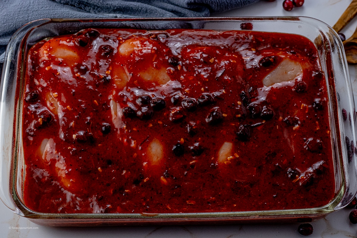 uncooked chicken in a glass baking dish in a cranberry sauce