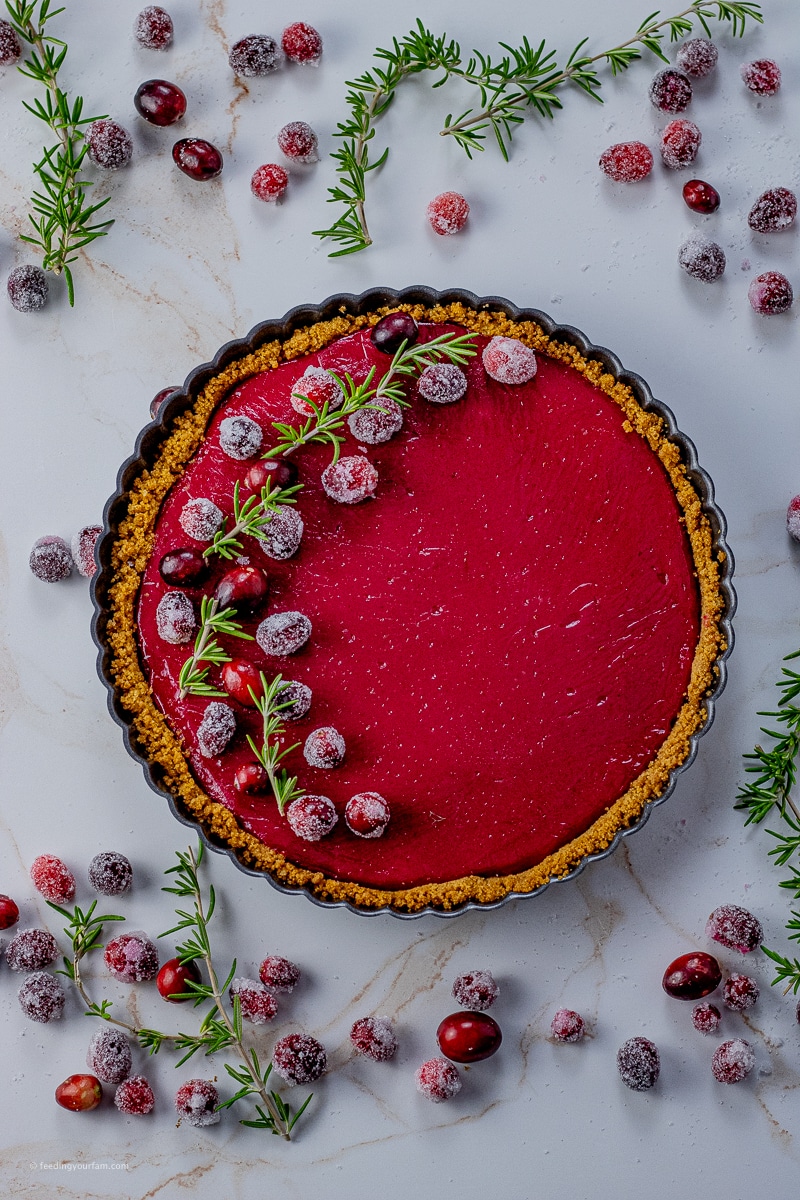 cranberry tart in a graham cracker crust in a tart pan, topped with sugared cranberries and rosemary sprigs