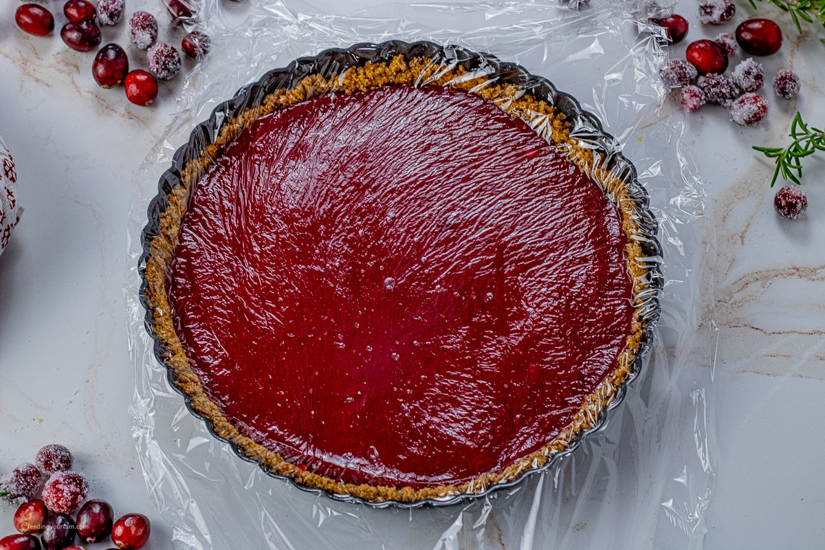 cranberry tart in a tart pan covered with a piece of plastic wrap