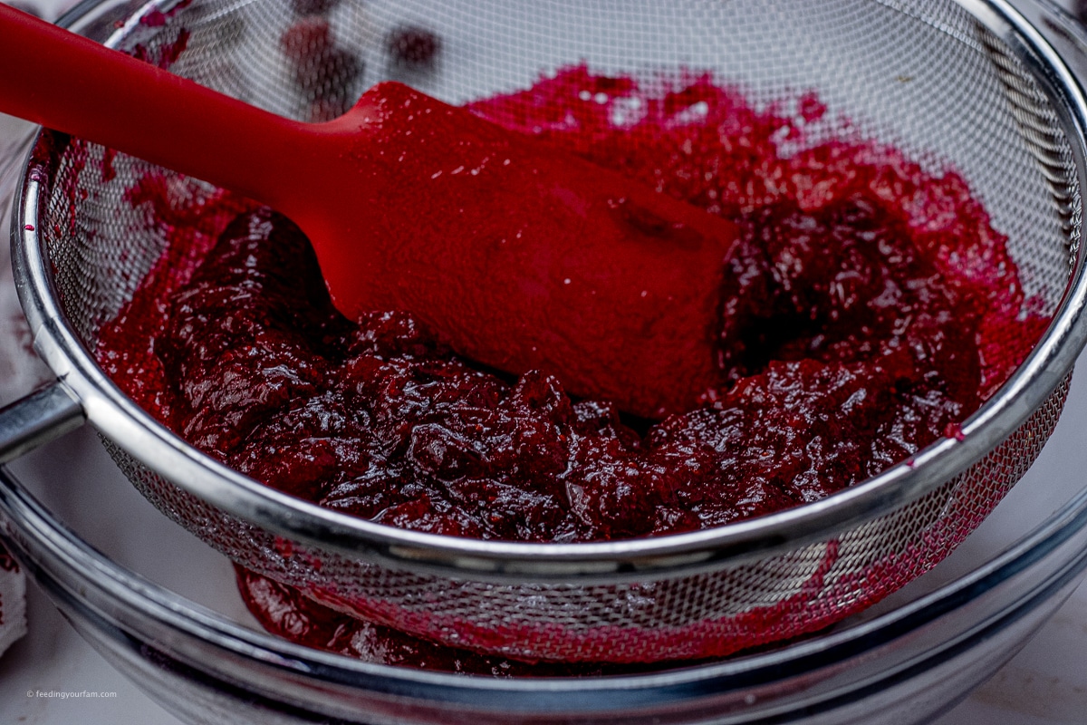 pressing cranberry curd mixture through a wire strainer with a red spatula