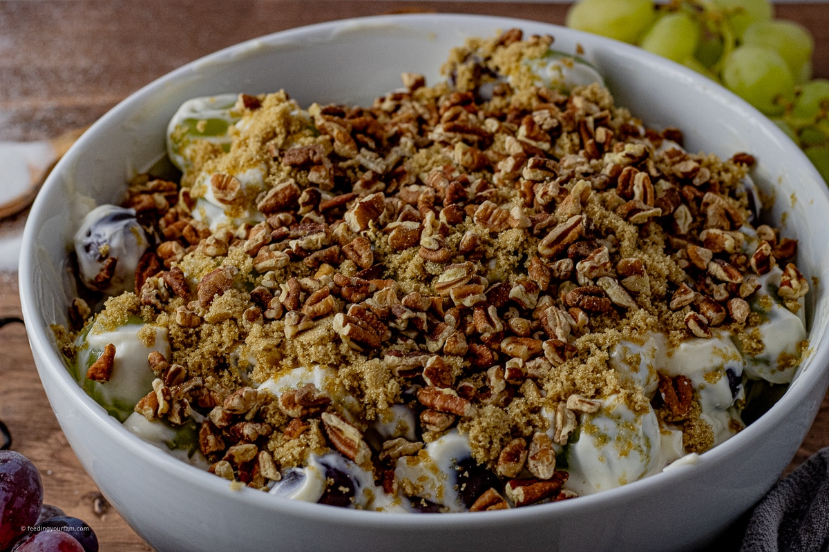 grape salad topped with brown sugar and pecans in a white serving bowl