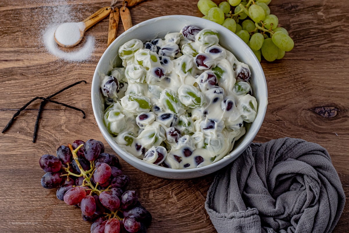 red and green grape salad topped with a cream cheese dressing in a white serving bowl