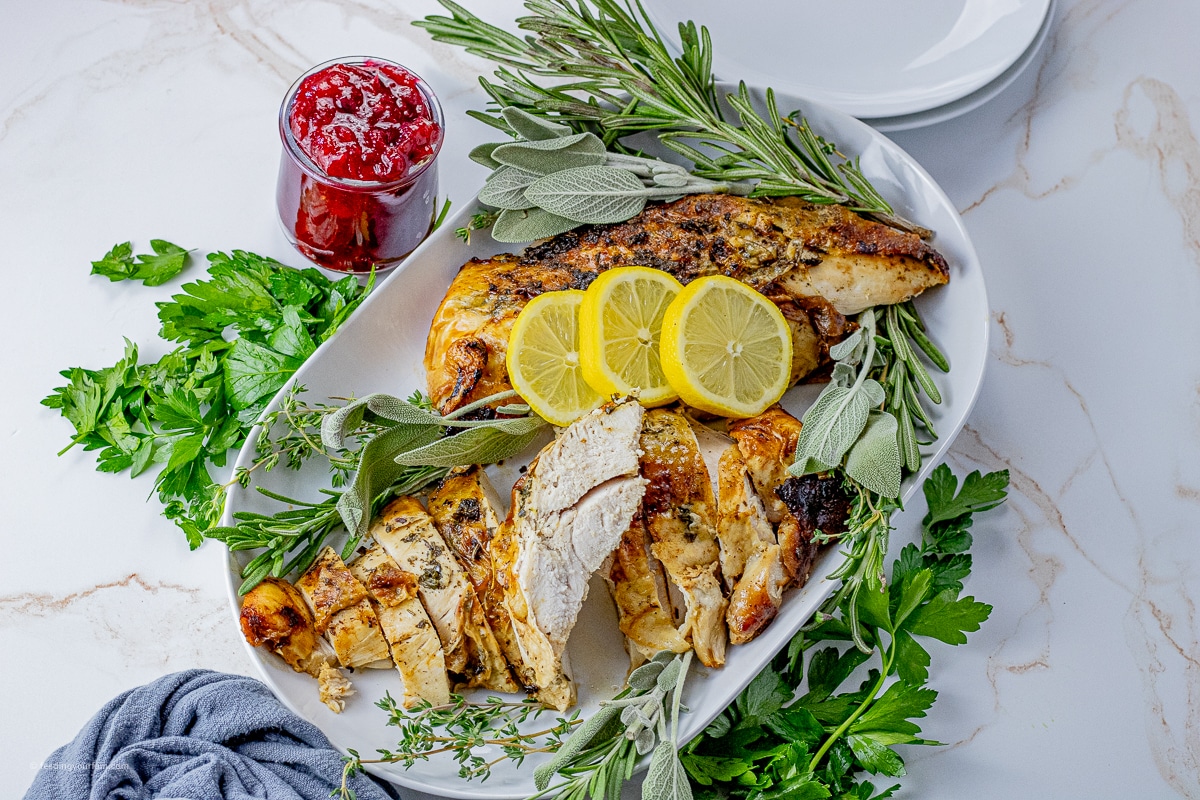 sliced turkey breast on a white serving platter with fresh herbs and lemon slices around it