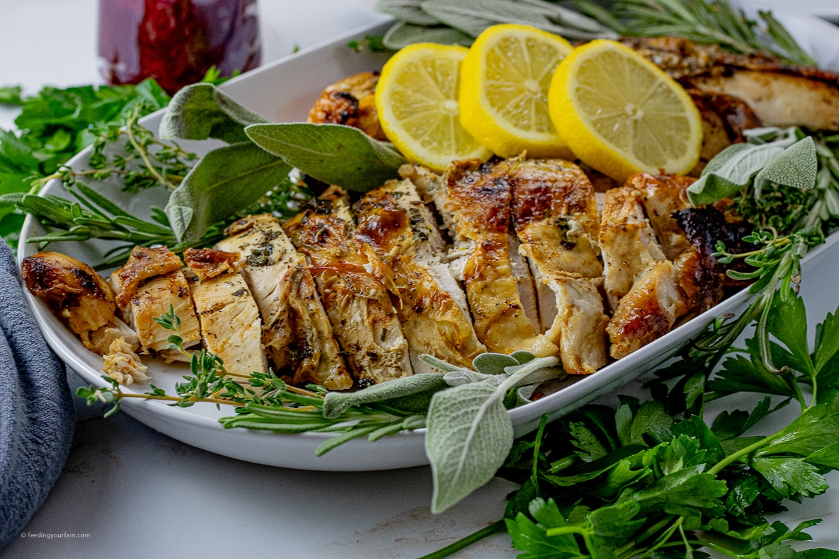 sliced, cooked turkey breast on a white serving platter with lemon slices and fresh herbs