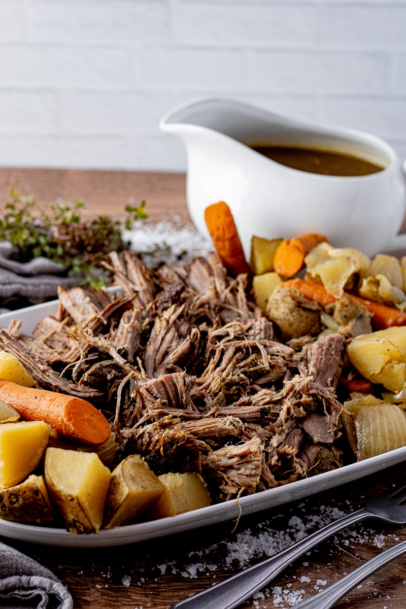 beef roast shredded into smaller pieces on a platter with carrots, onions and potatoes