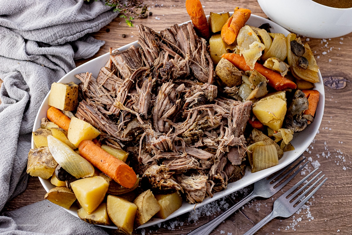 pot roast that has been shredded and placed on a platter with carrots and potatoes