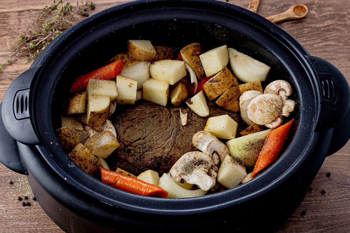beef roast surrounded with potatoes, onions, mushrooms and carrots in a slow cooker