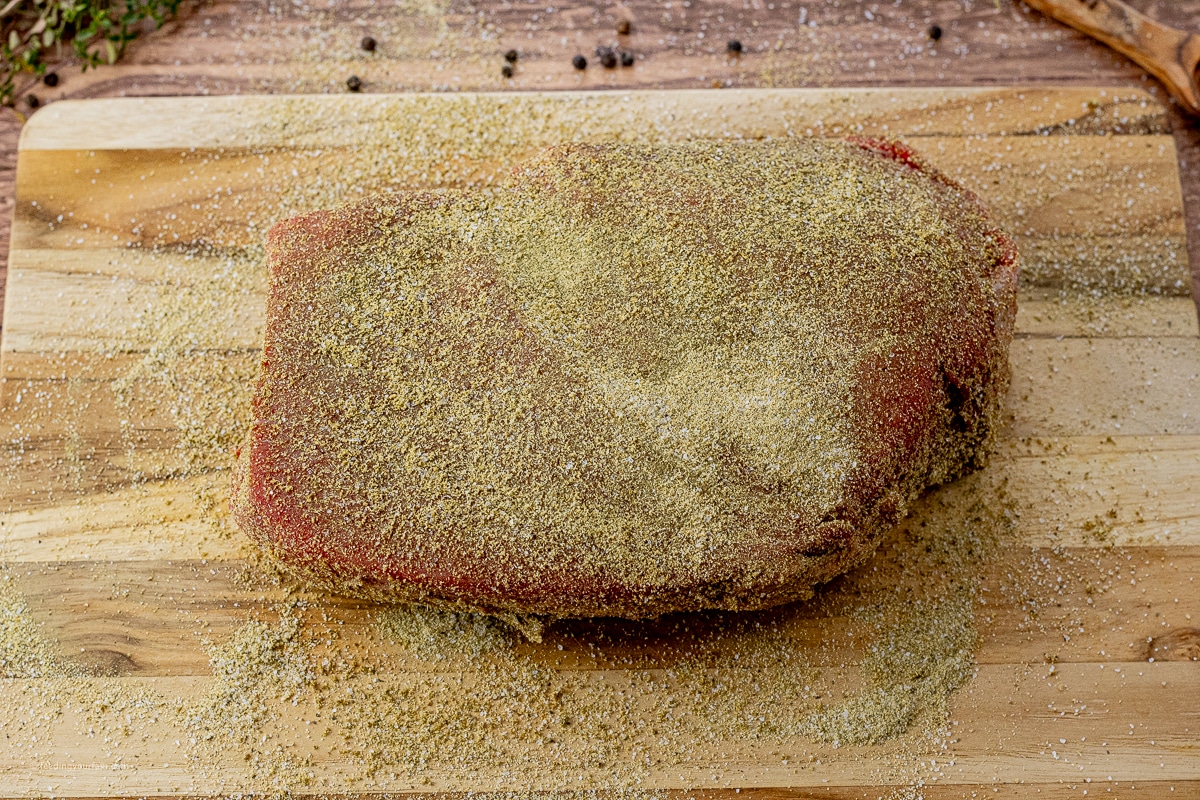 uncooked beef roast with seasoning all over it on a wooden cutting board