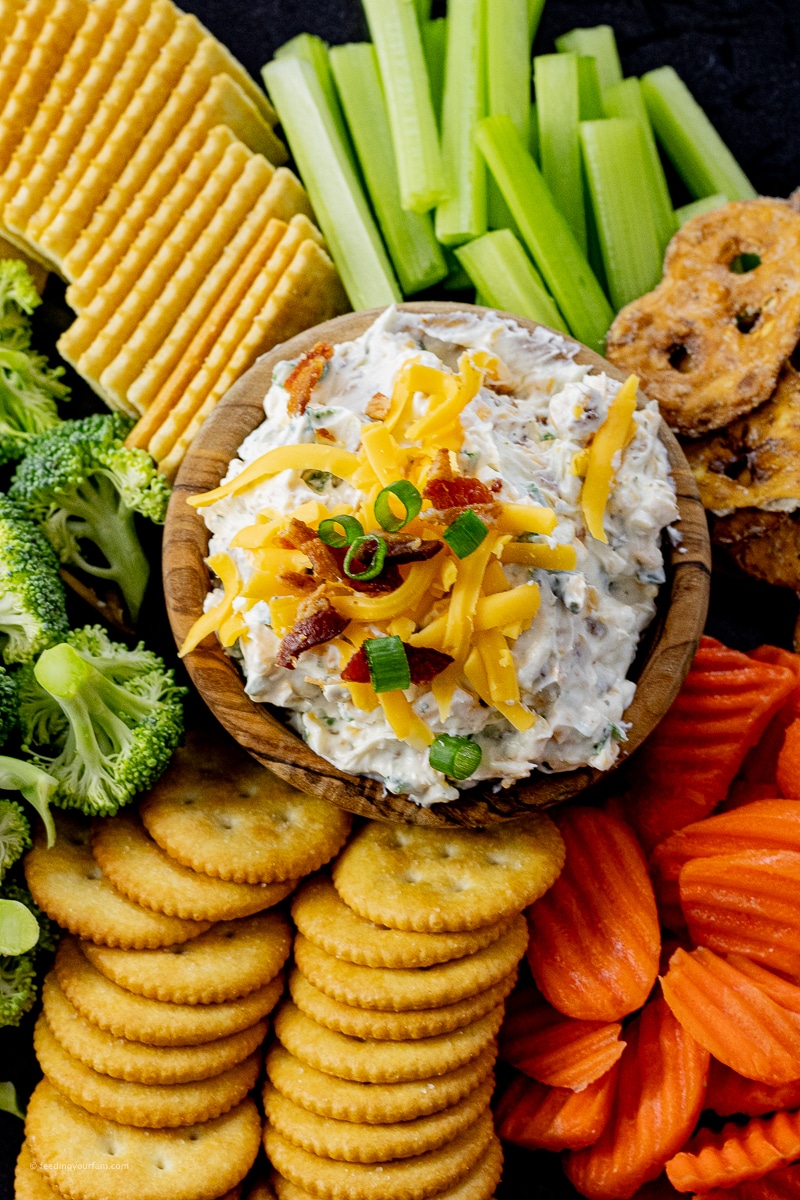 cream cheese dip made with ranch, bacon and green onions in a bowl served with crackers and vegetables