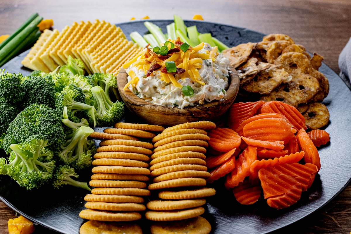 dip made with cream cheese and topped with bacon and cheese served with crackers and vegetables
