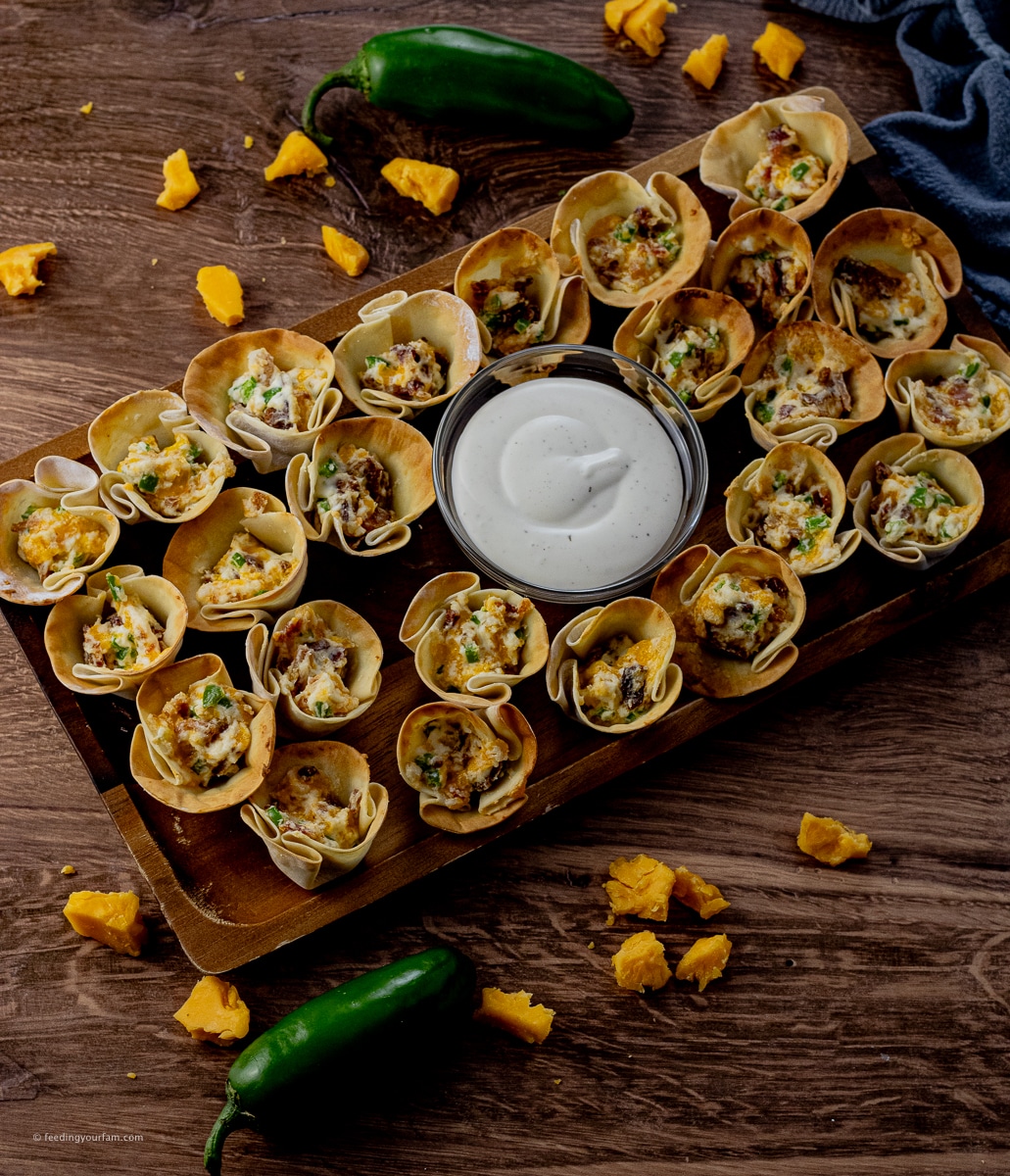 gyoza cups filled with jalapeno popper filling with a bowl of ranch dressing in the middle